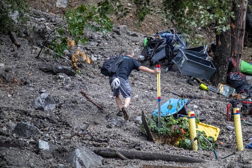 FOREST FALLS, CA - SEPTEMBER 12, 2022: Homeowner Olin Richie steadies himself on a metal pole while trying to hike up to his house through mud and debris after heavy rain created a large mudslide on Canyon Drive on September 12, 2022 in Forest Falls, California. (Gina Ferazzi / Los Angeles Times)