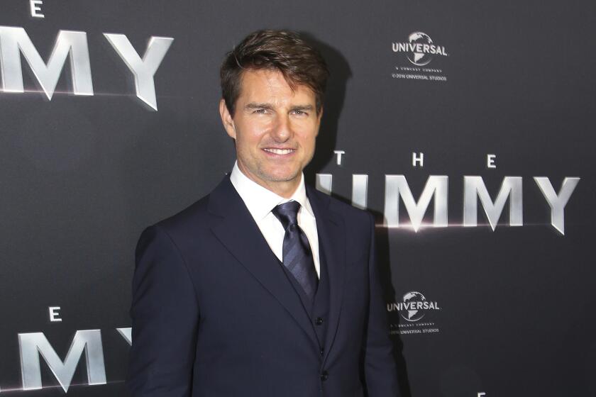 Tom Cruise smiling in a dark blue suit and tie and white shirt before a movie premiere