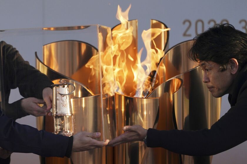 FILE - In this March 25, 2020, file, photo, officials light a lantern from the Olympic Flame at the end of a flame display ceremony in Iwaki, northern Japan. Before the Olympics were postponed, Japan looked like it had coronavirus infections contained, even as they spread in neighboring countries. Now that the games have been pushed to next year, Tokyo’s cases are spiking, and the city's governor is requesting that people stay home, even hinting at a possible lockdown. (AP Photo/Eugene Hoshiko, File)