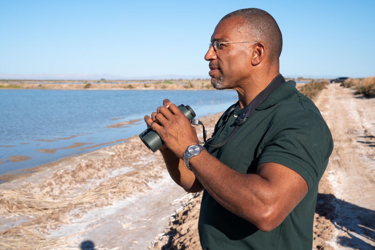 A man holding binoculars stands on a seashore