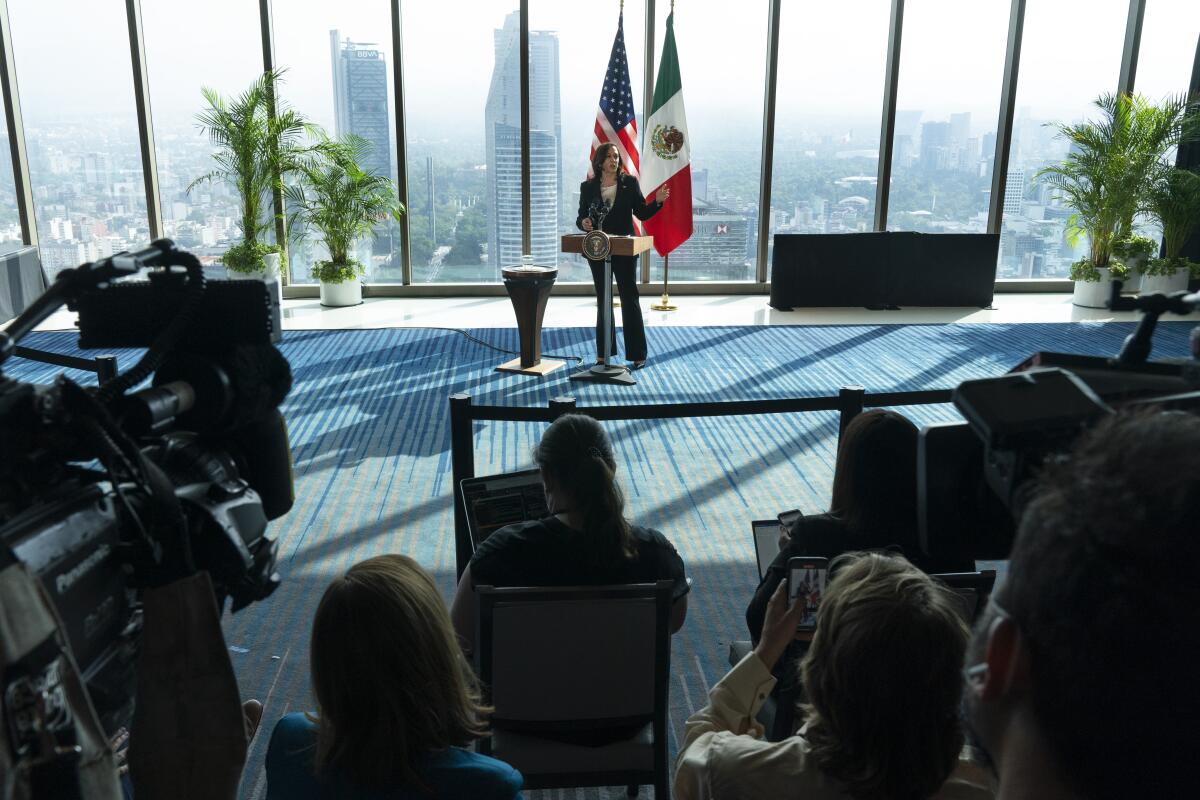 Vice President Kamala Harris speaks to reporters with the foggy Mexico City skyline in tall windows behind her