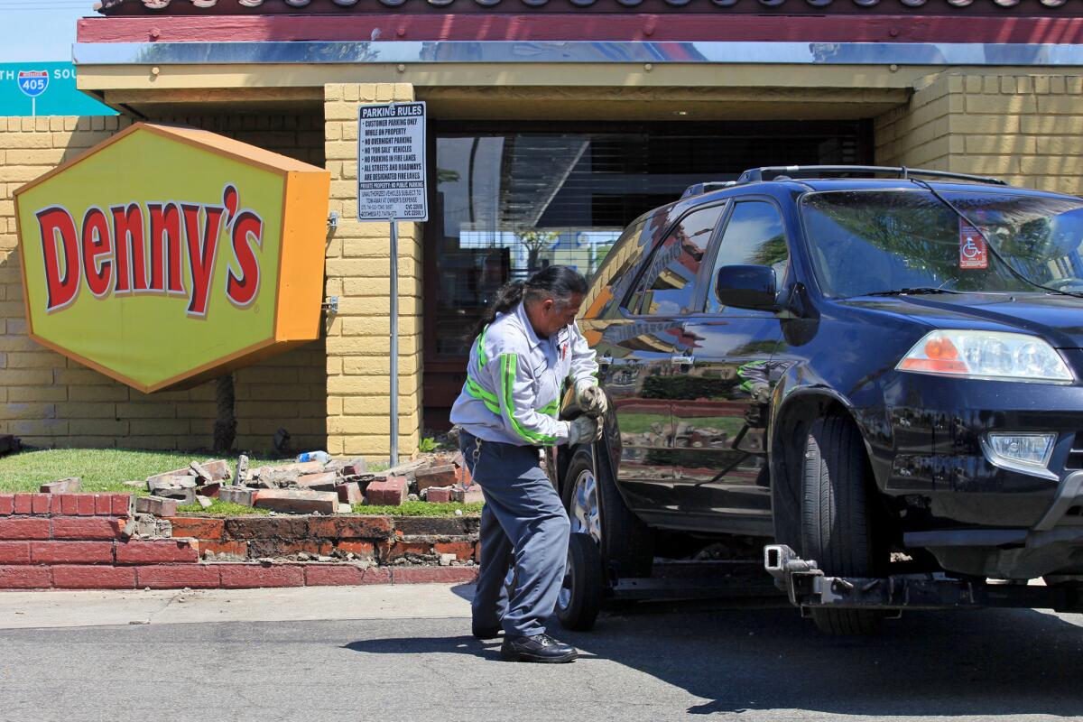 A tow truck driver removes a black SUV after the driver backed into the Denny's diner along north Harbor Boulevard on Tuesday in Costa Mesa.