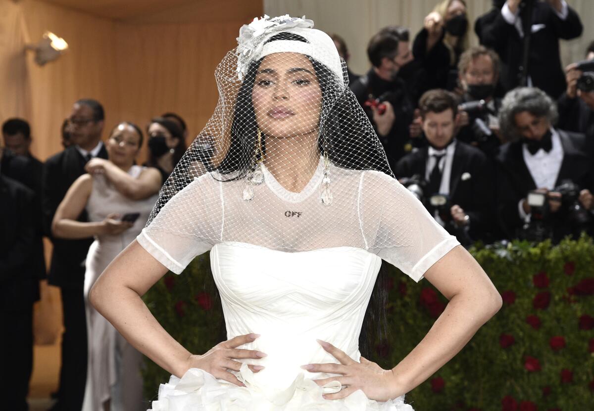 A woman in a white dress, white veil and baseball cap posing with her hands on her hips