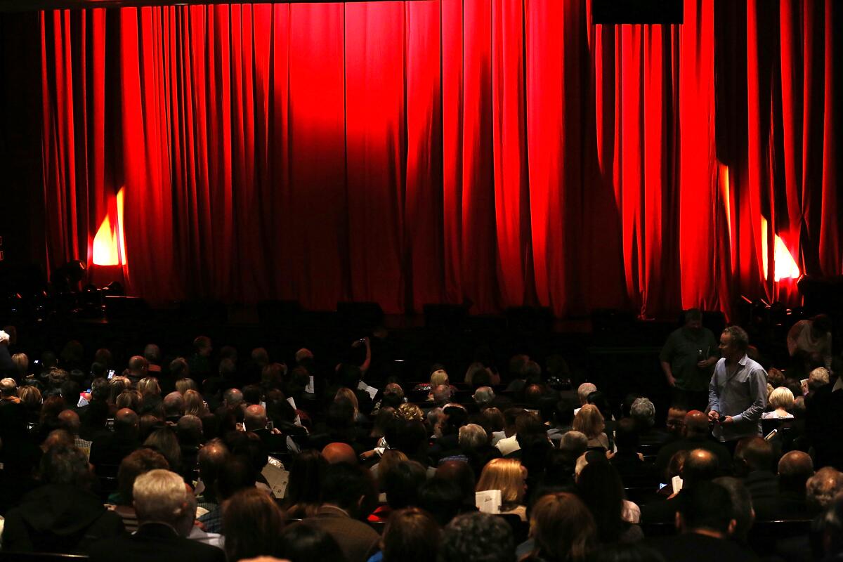 An audience waits for the red curtain in front of them to open at a theater
