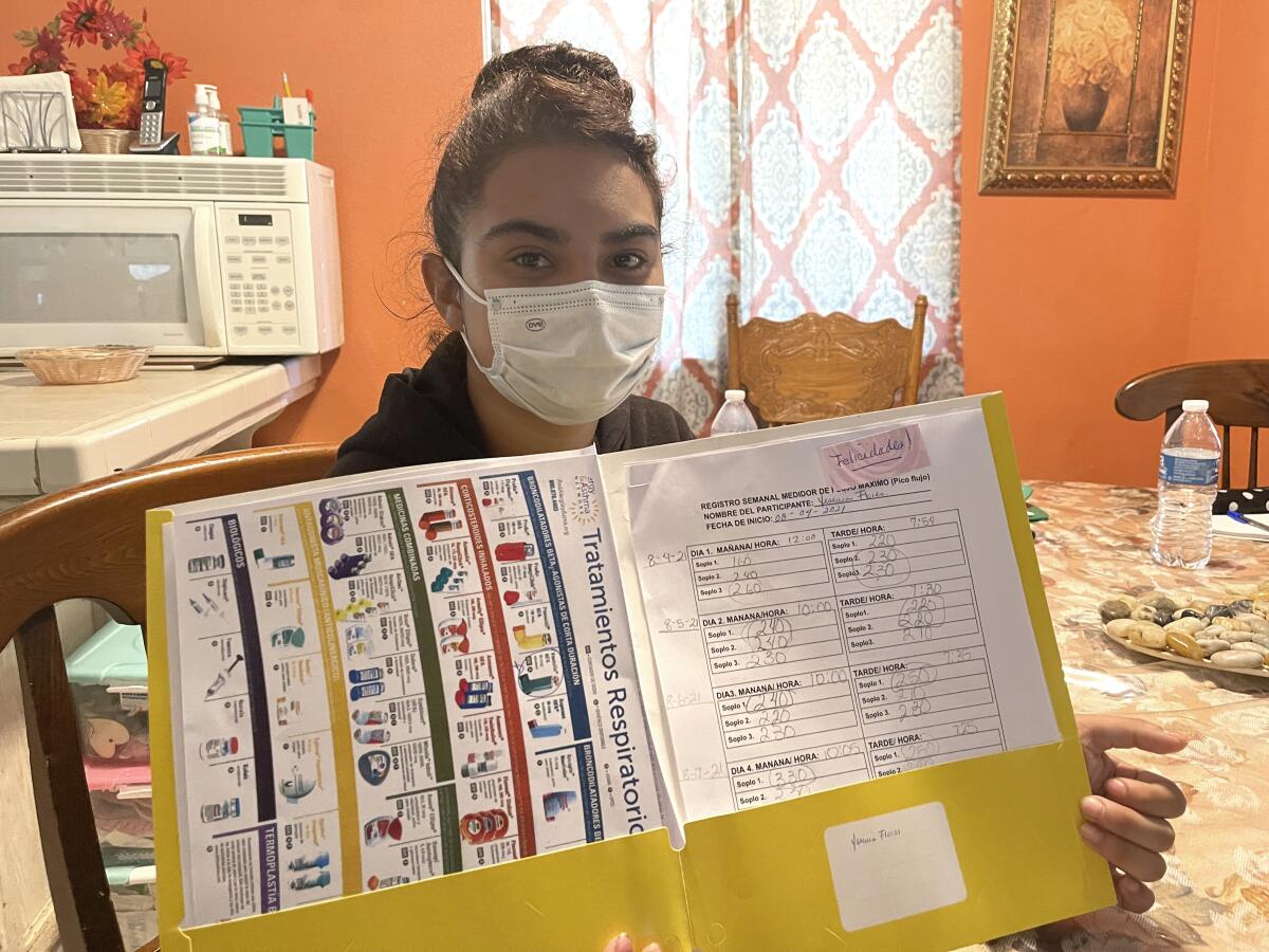 A girl wearing a face mask holds up a yellow folder holding charts and diagrams 
