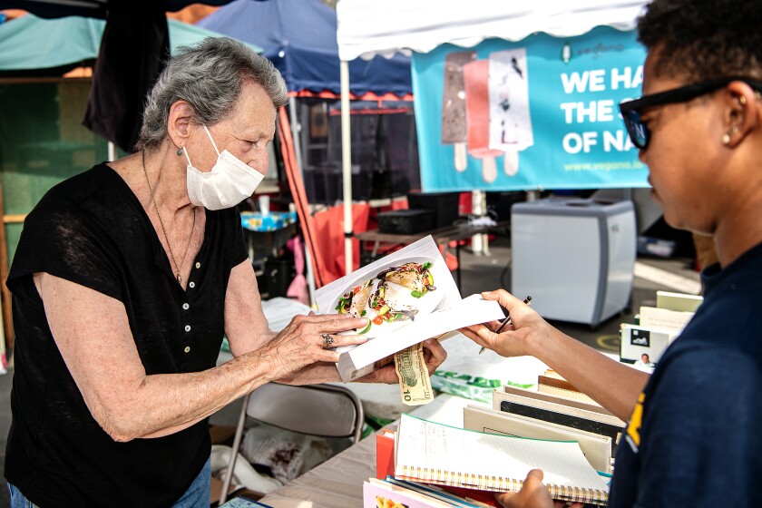 A woman holding a $10 bill flips through a cookbook as a man looks on.