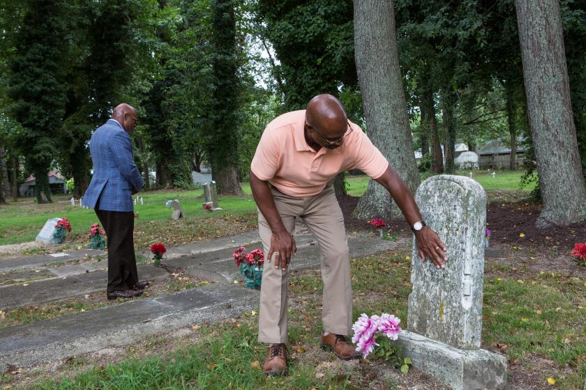 Vincent Tucker traces the almost invisible name of his ancestor, Mary E. Tucker, in the Tucker Family Graveyard in Hampton, Va. her tombstone is dated 1856. His brother, Verrandall Tucker is at left.