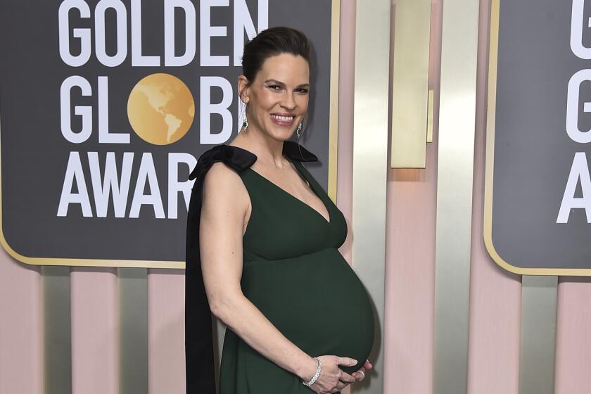A pregnant Hilary Swank smiles while wearing a green gown and cradling her baby bump