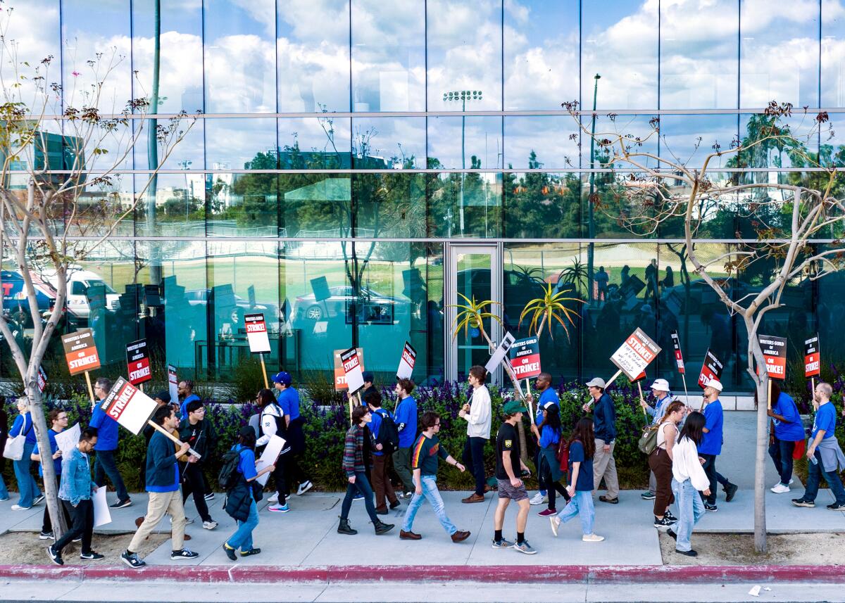 People holding up pickets walk in front of the glass front of a building.