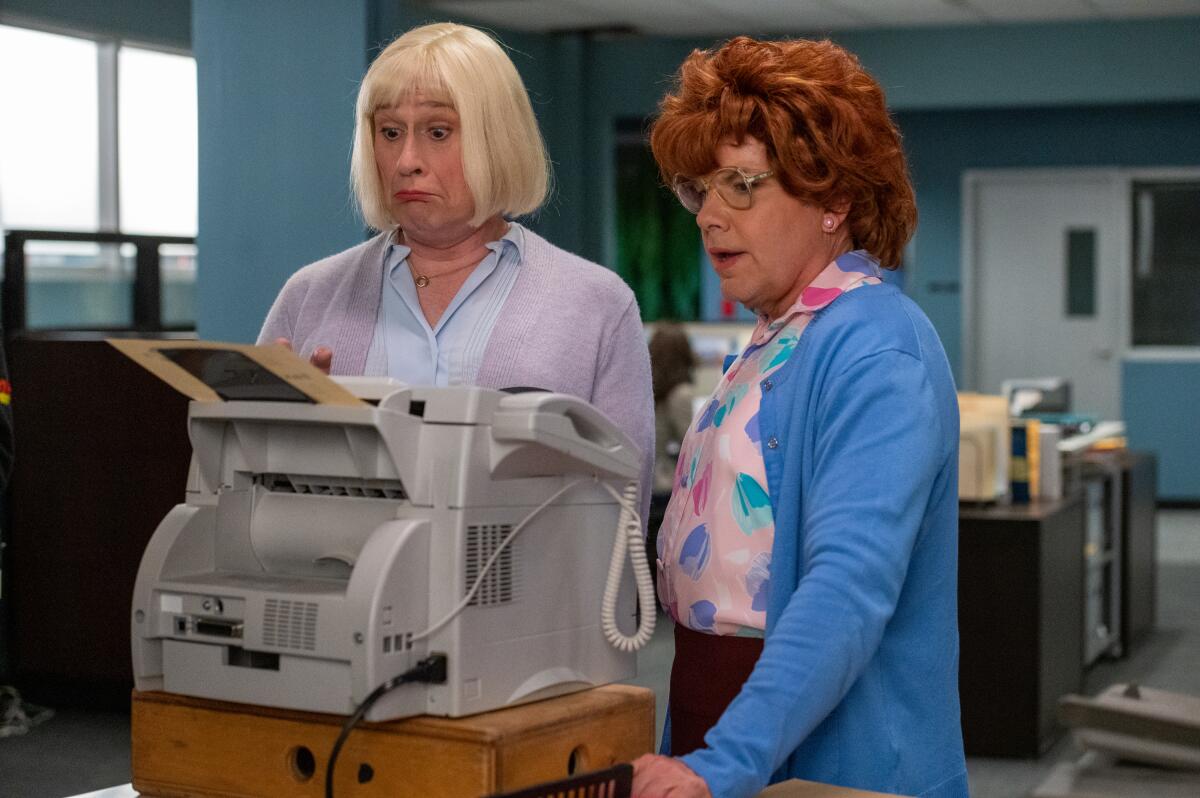 Two men dressed as women operating a fax machine.