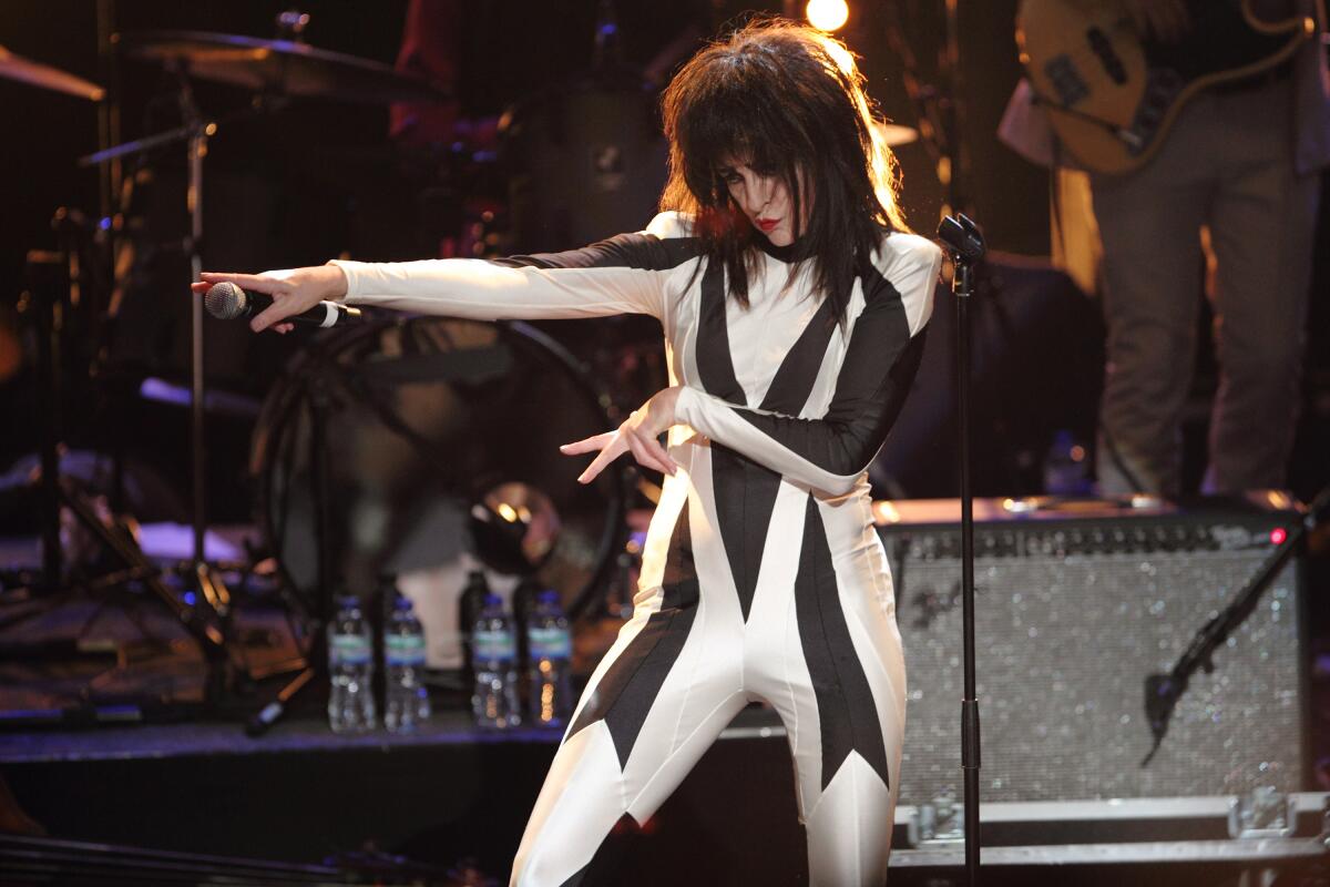 Siouxsie Sioux onstage in a black and white bodysuit, pointing and gesturing