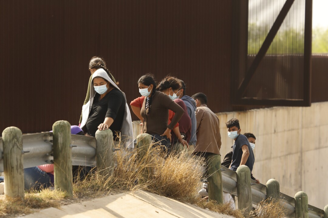 Asylum seekers sit on a metal guardrail alongside a barrier