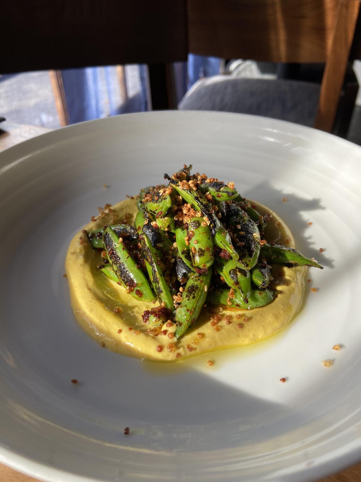 A bowl of yellow labneh topped with a small mound of snap peas on a table.