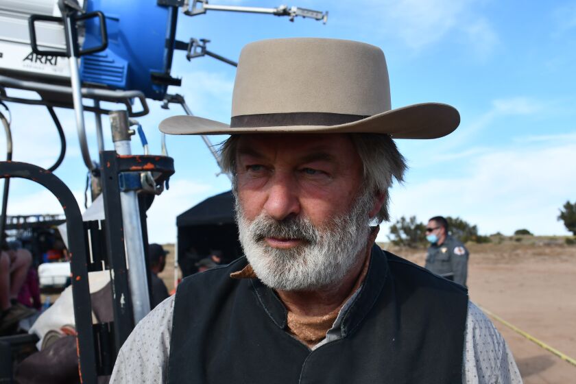A man with a white beard wearing a hat stands on a movie set
