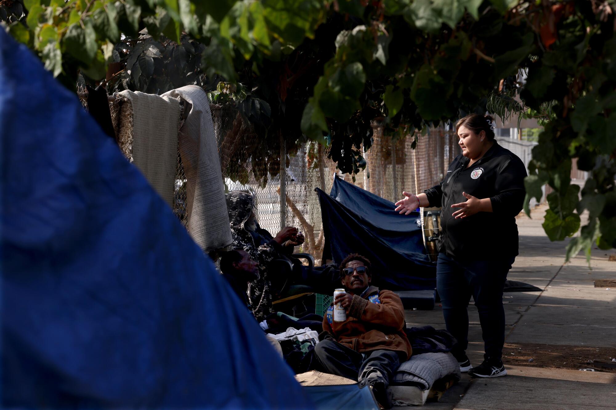 A woman speaks to people in an encampment. 