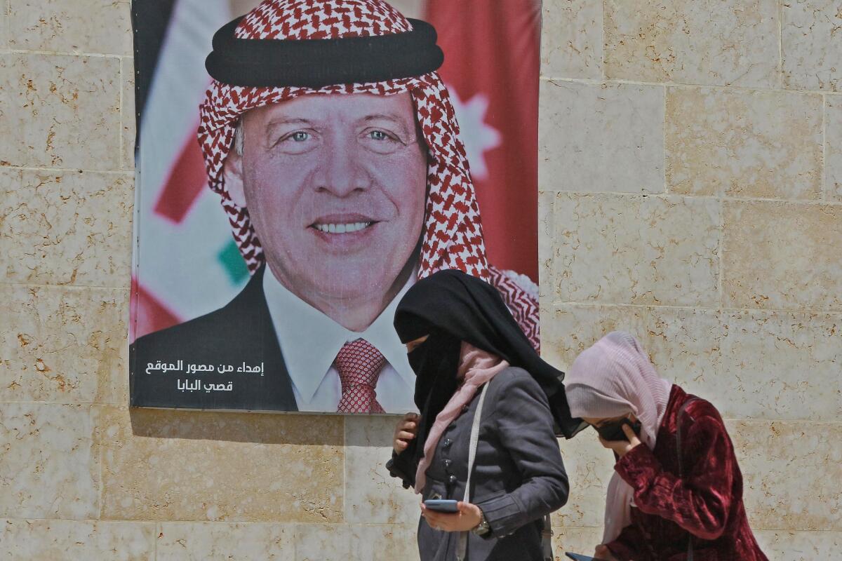 Women walk past a poster of Jordan's King Abdullah II on a street in the capital Amman.