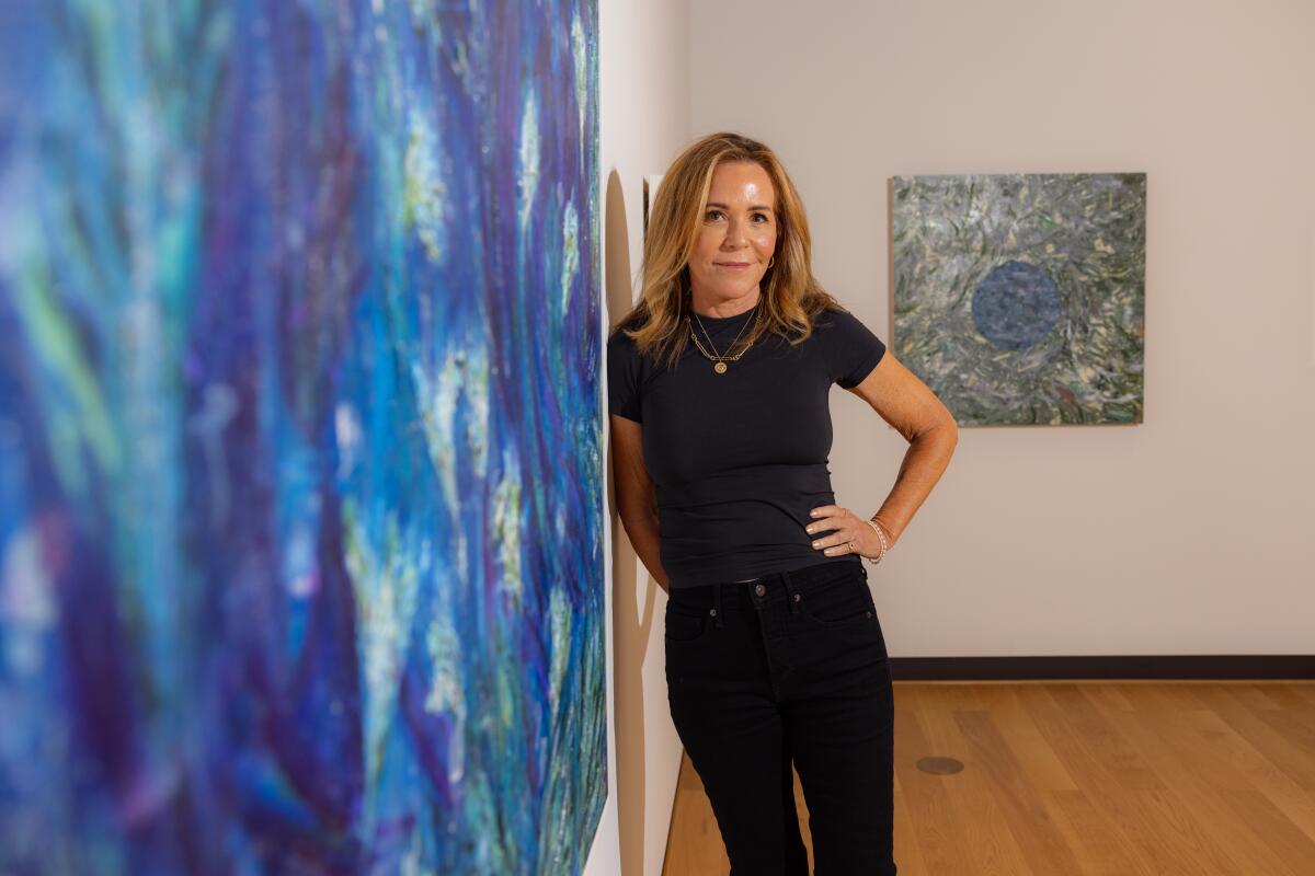 Denise Di Novi stands next to one of her paintings, an abstract  swirl of blues and greens.