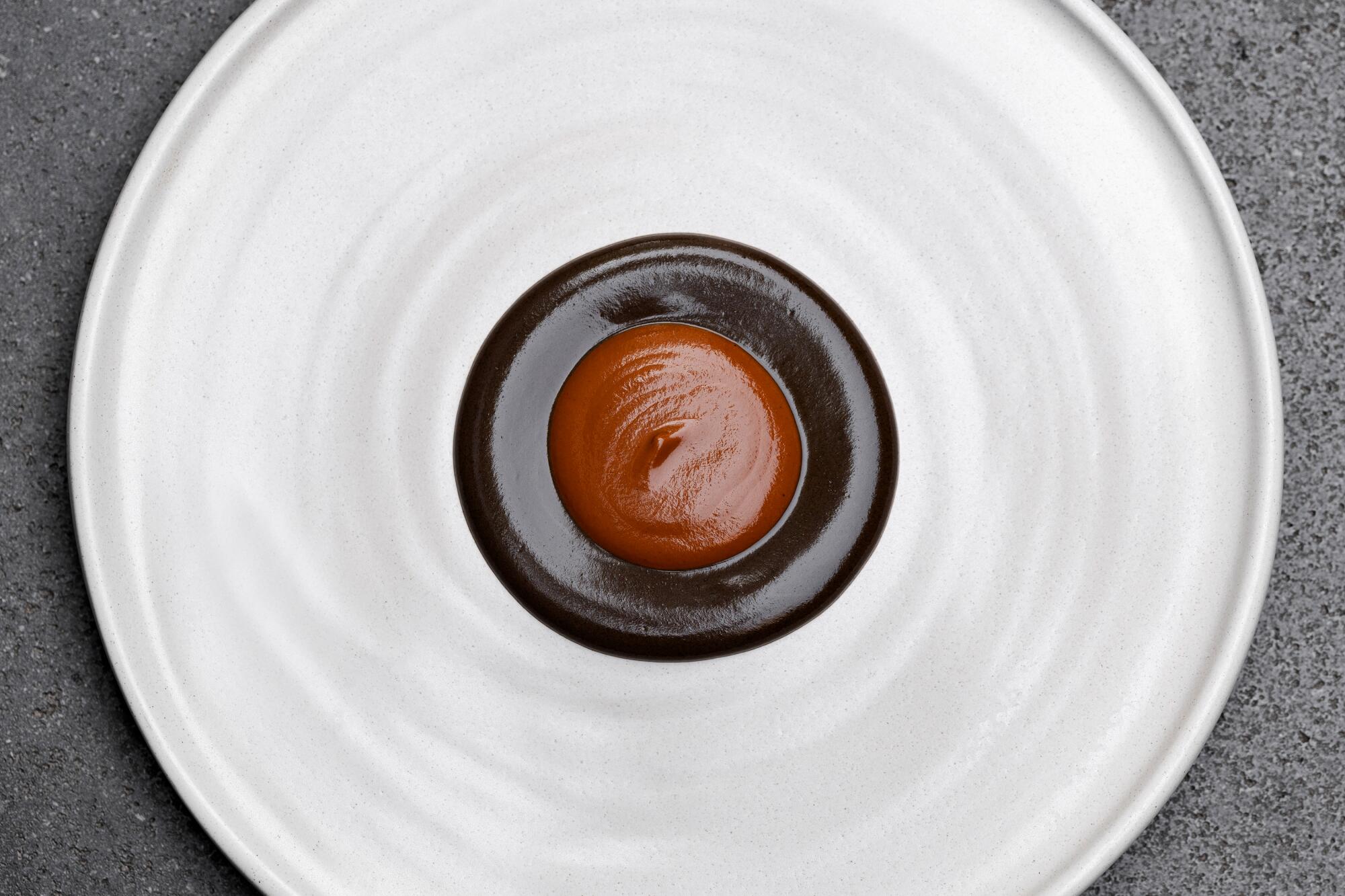 A plate with a reddish sauce and a brown sauce centered