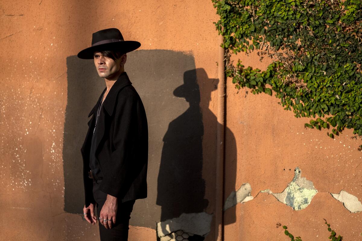 Actor Andrew Diego wears black and stands before an earth colored wall in late afternoon light
