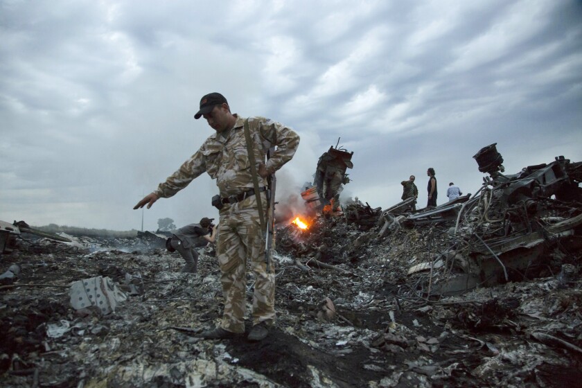 FILE- In this July 17, 2014, file photo, people walk amongst the debris at the crash site of MH17 passenger plane near the village of Grabovo, Ukraine, that left 298 people killed. A lawyer for relatives of people killed in the 2014 downing of Malaysia Airlines Flight 17 over eastern Ukraine told a court hearing Thursday, April 15, 2021 that 290 family members and partners of the victims have filed compensation claims for “emotional distress" against four suspects charged in the downing. (AP Photo/Dmitry Lovetsky, File)