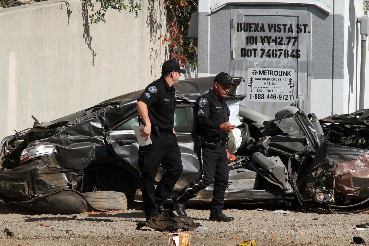 Two Burbank police officers walk past a car hit by a train at the intersection of San Fernando Boulevard and Buena Vista Street in Burbank.