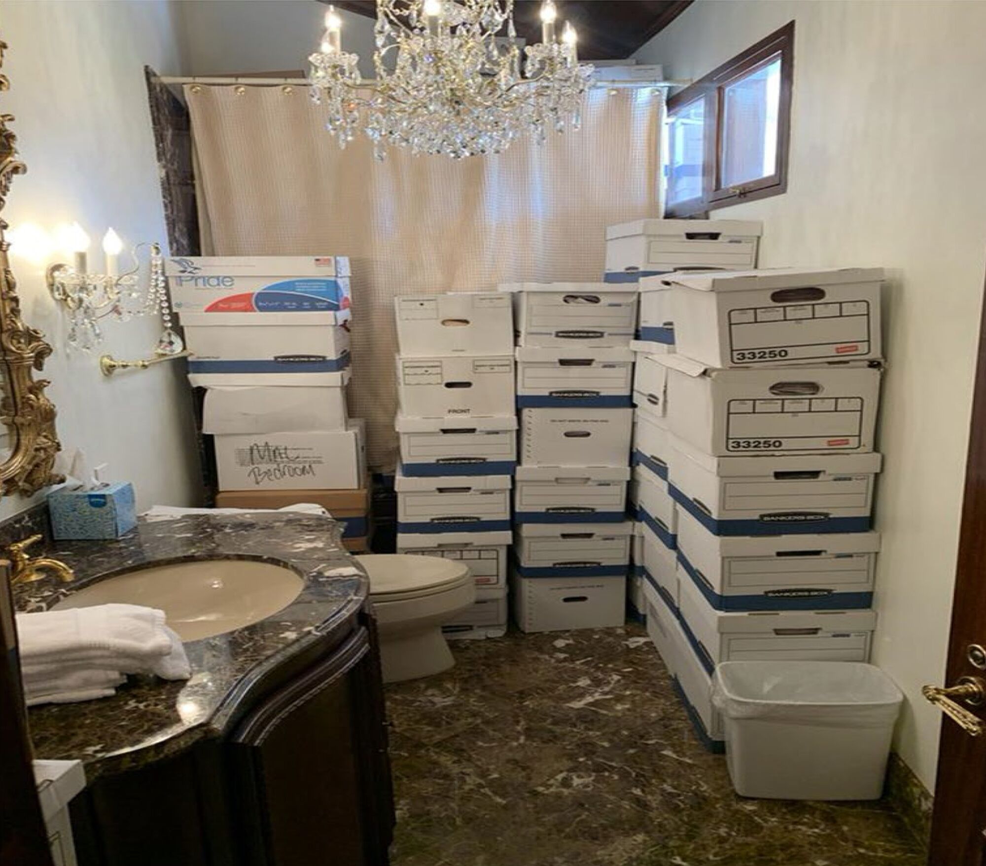 An interior frame of a bathroom with stacks of paper boxes against the wall at right and back against the shower curtain