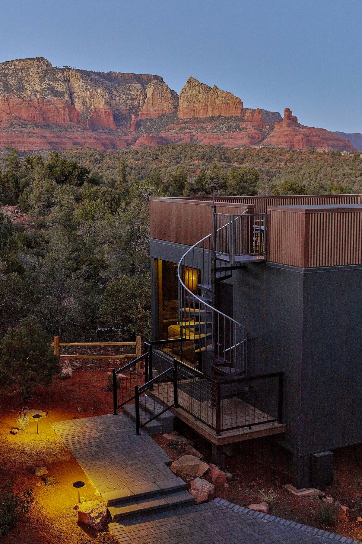 A building with a spiral staircase to its roof, against a backdrop of red rock mountains