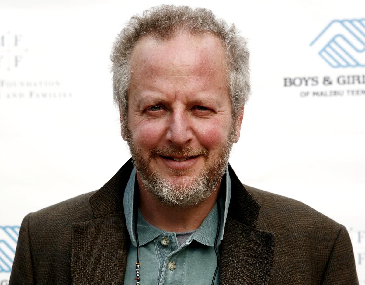 Daniel Stern, with a collared shirt, brown blazer and white beard, smiles into the camera.
