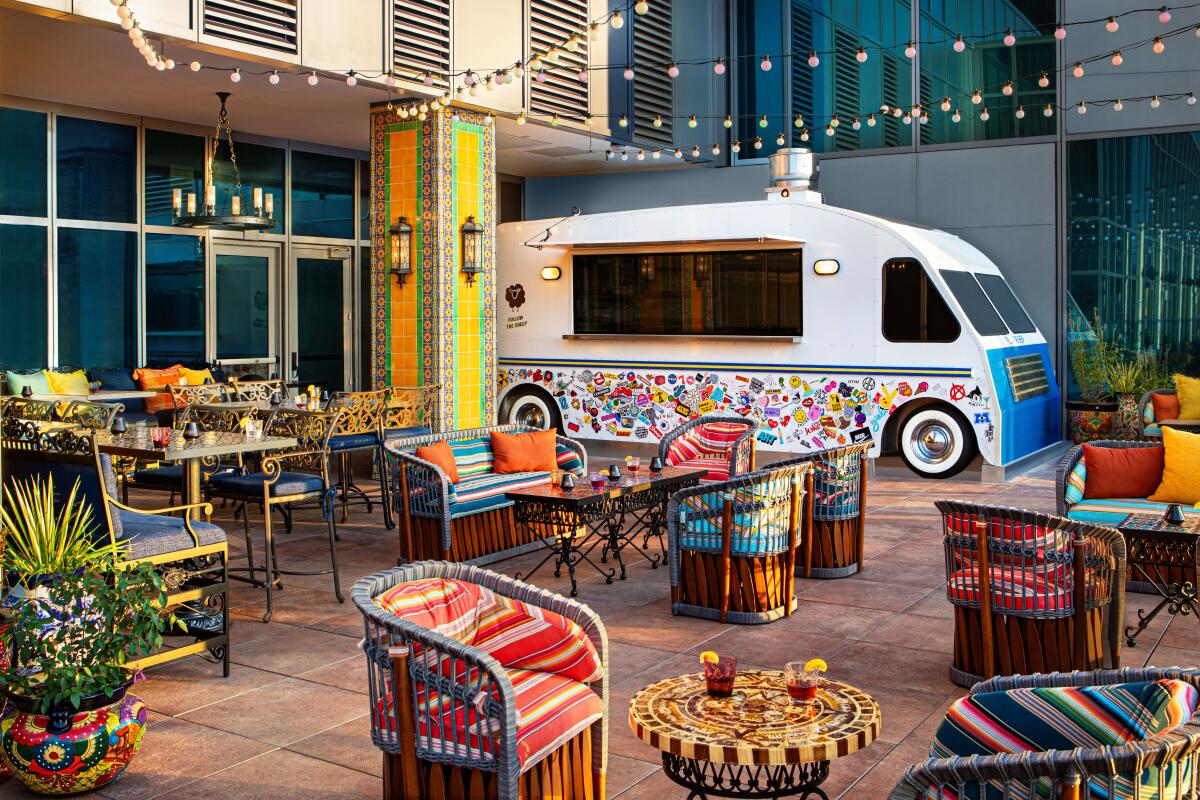 A white faux food truck parked next to a colorfully furnished and decorated patio.