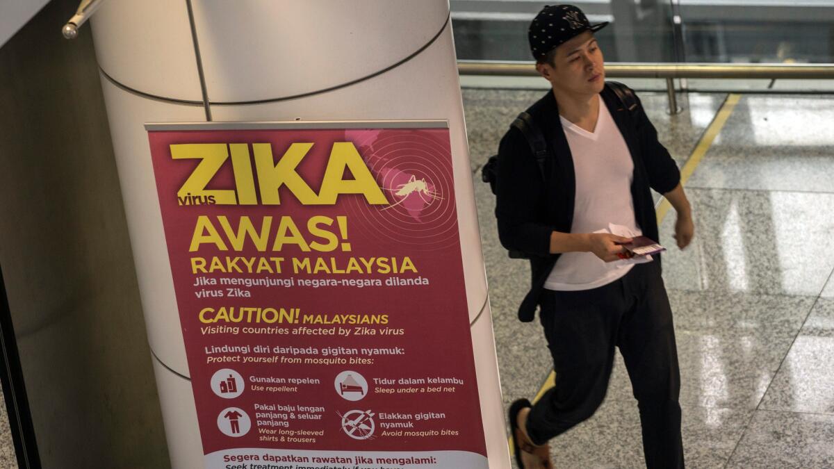 A traveler walks near a travel advisory poster providing information on the zika virus at Kuala Lumpur International Airport in Sepang, Malaysia.