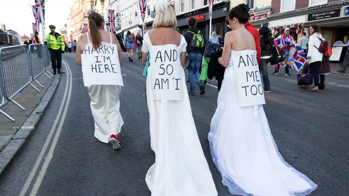 Women wearing wedding dresses and signs for Prince Harry are part of the crowd for the royal wedding in Windsor, England, on May 19.