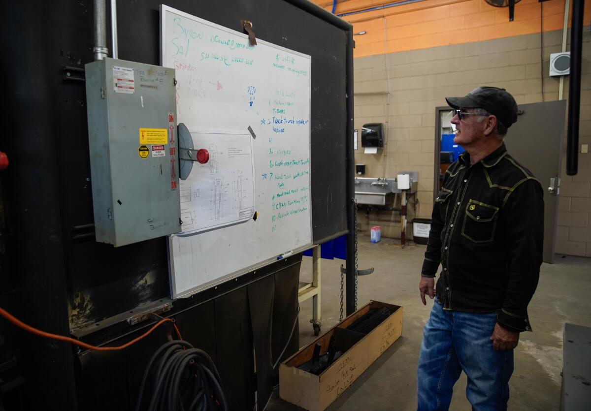 A man in a welding studio looks at a whiteboard.