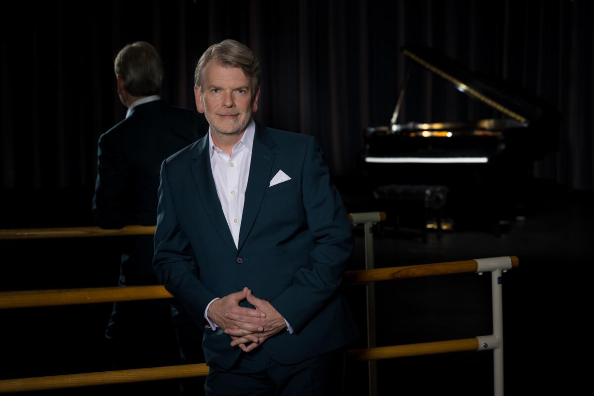 A man wearing a blue suit with an open-collared white shirt.