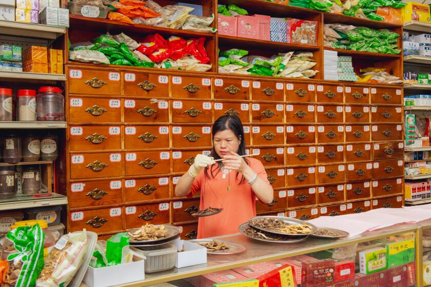 Los Angeles, CA- March 4: Shop clerk, Angela He, using the traditional copper weighted herb scale for dispensing herbs at Tian Xiang Chinese herbal medicine clinic on Saturday March 4, 2024 in Los Angeles, CA. Jason LeCras for The LA Times.