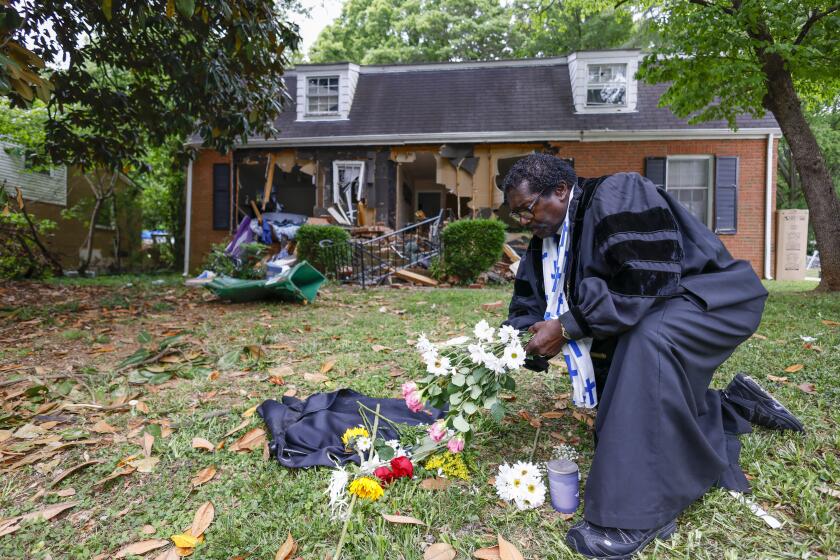 Rev. Raymond Johnson, of Marion, S.C., arranges flowers on the lawn of the home on Galway Drive in Charlotte, N.C., Tuesday, April 30, 2024 where a shootout between a suspect and officers occurred during an attempt to serve a warrant on Monday. Four law enforcement officers were killed. (AP Photo/Nell Redmond)