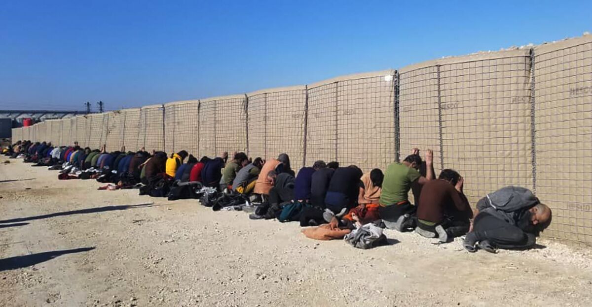 Islamic State group fighters kneel along a fence