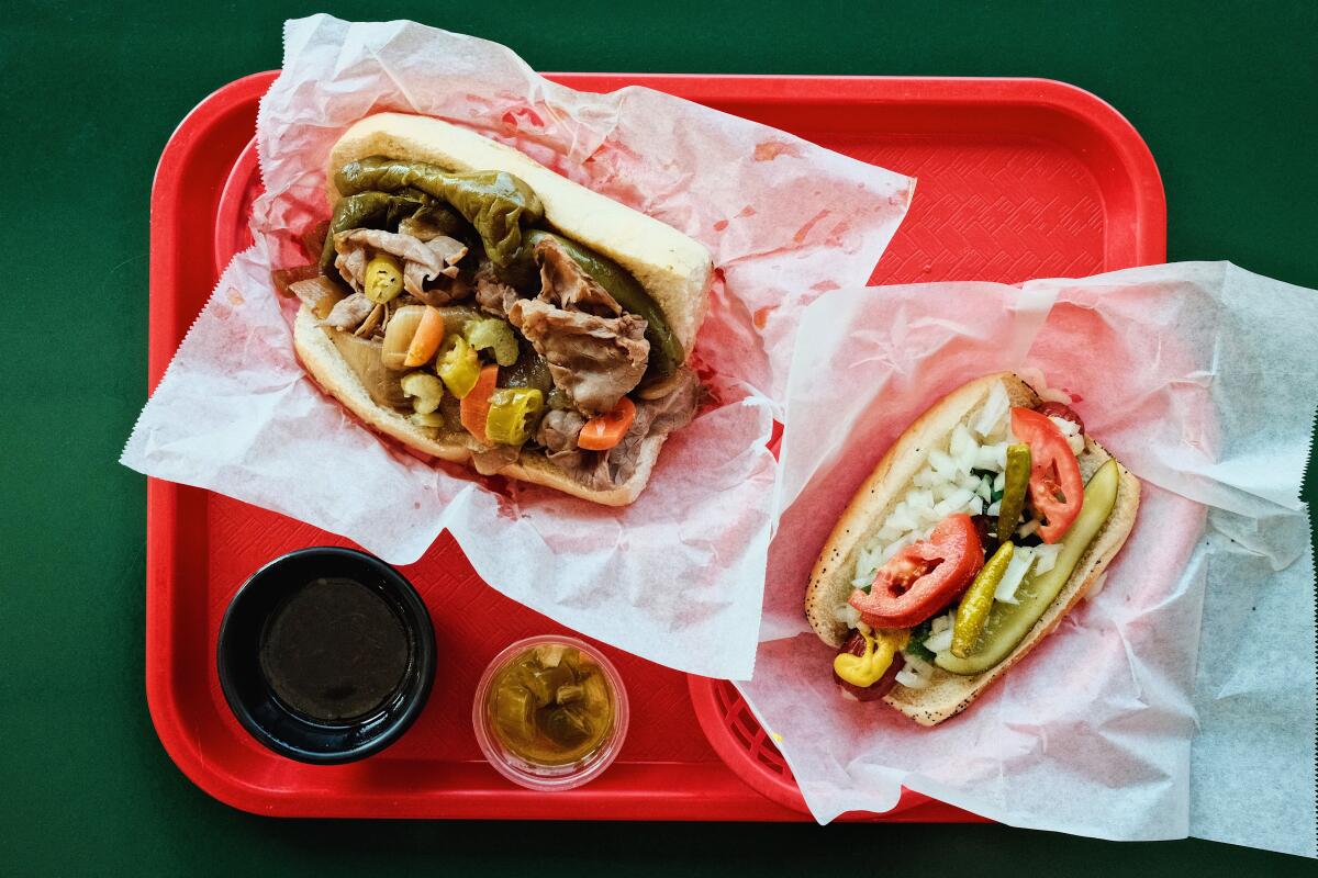 An Italian beef sandwich and a Chicago dog on a red tray on a green table at Mustard's Chicago Style Eatery in Los Alamitos.