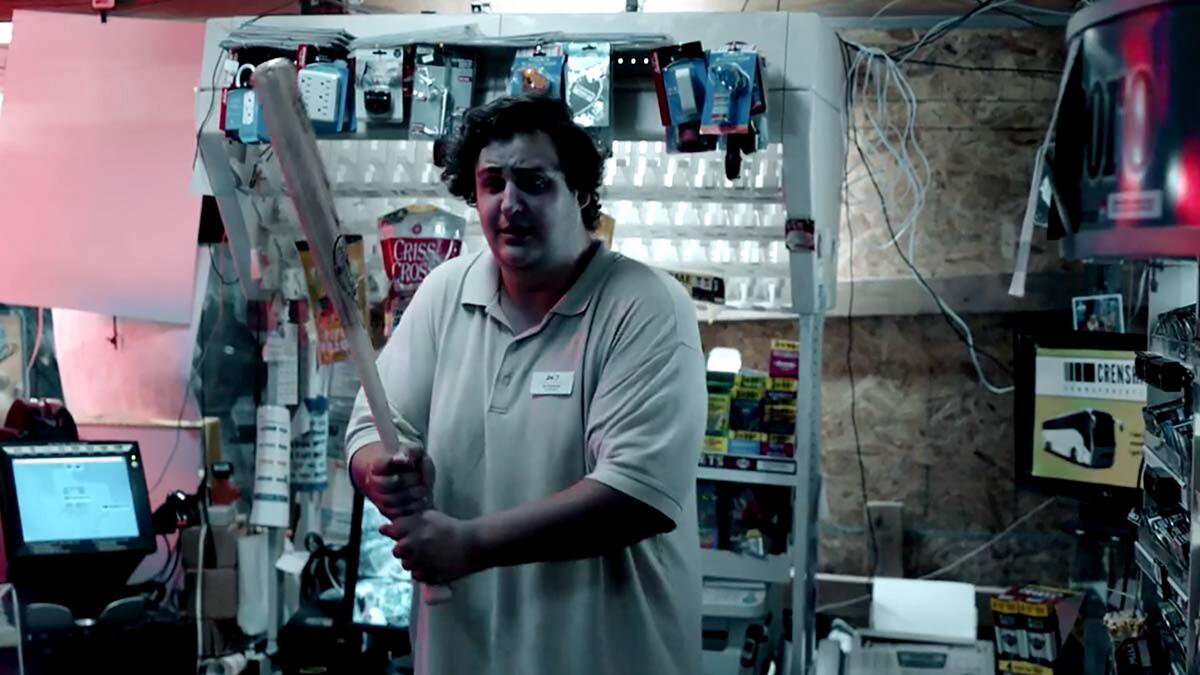 A man holds a baseball bat in a defensive manner inside a shop.