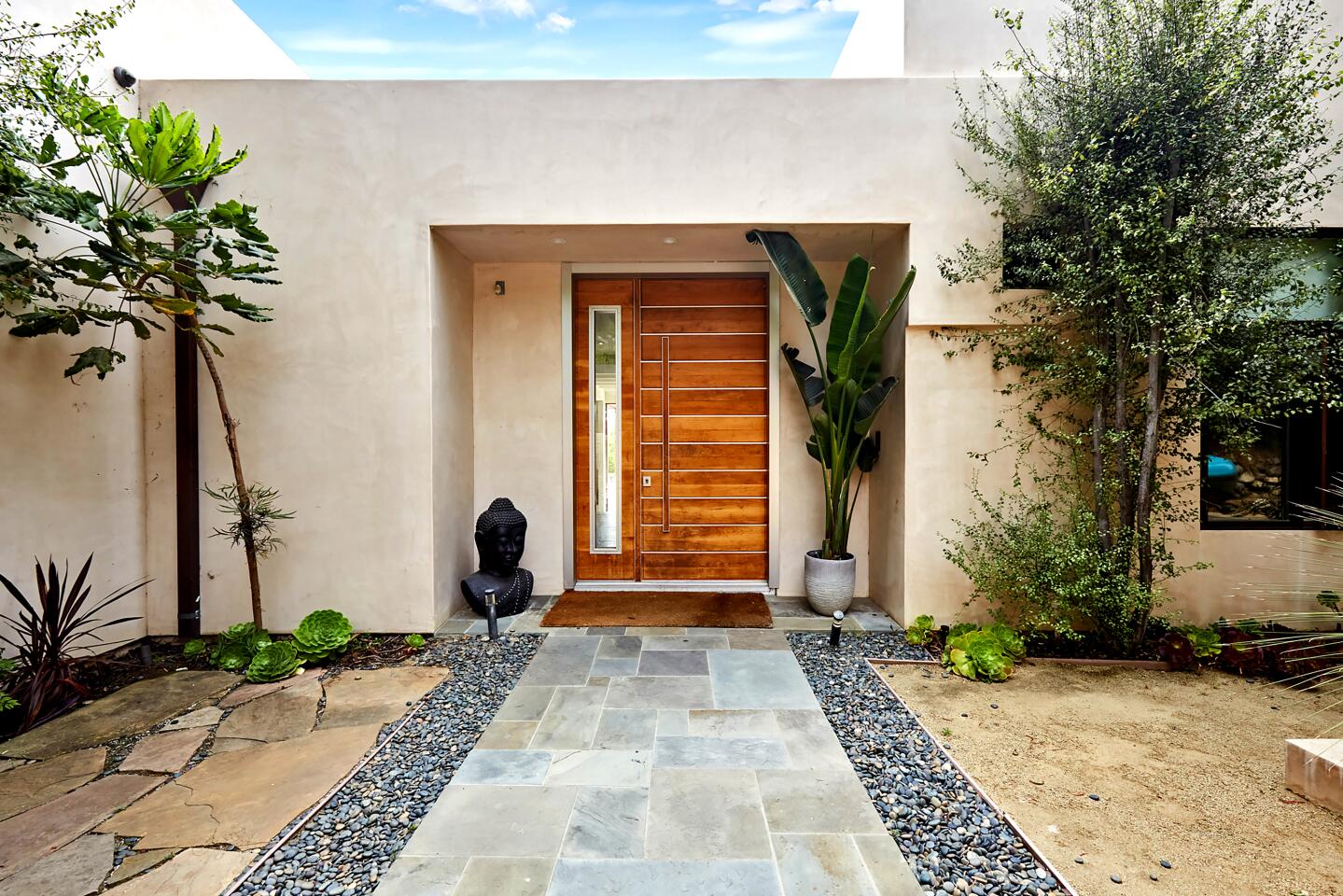 View of the front entrance wooden door and foliage from the walkway.