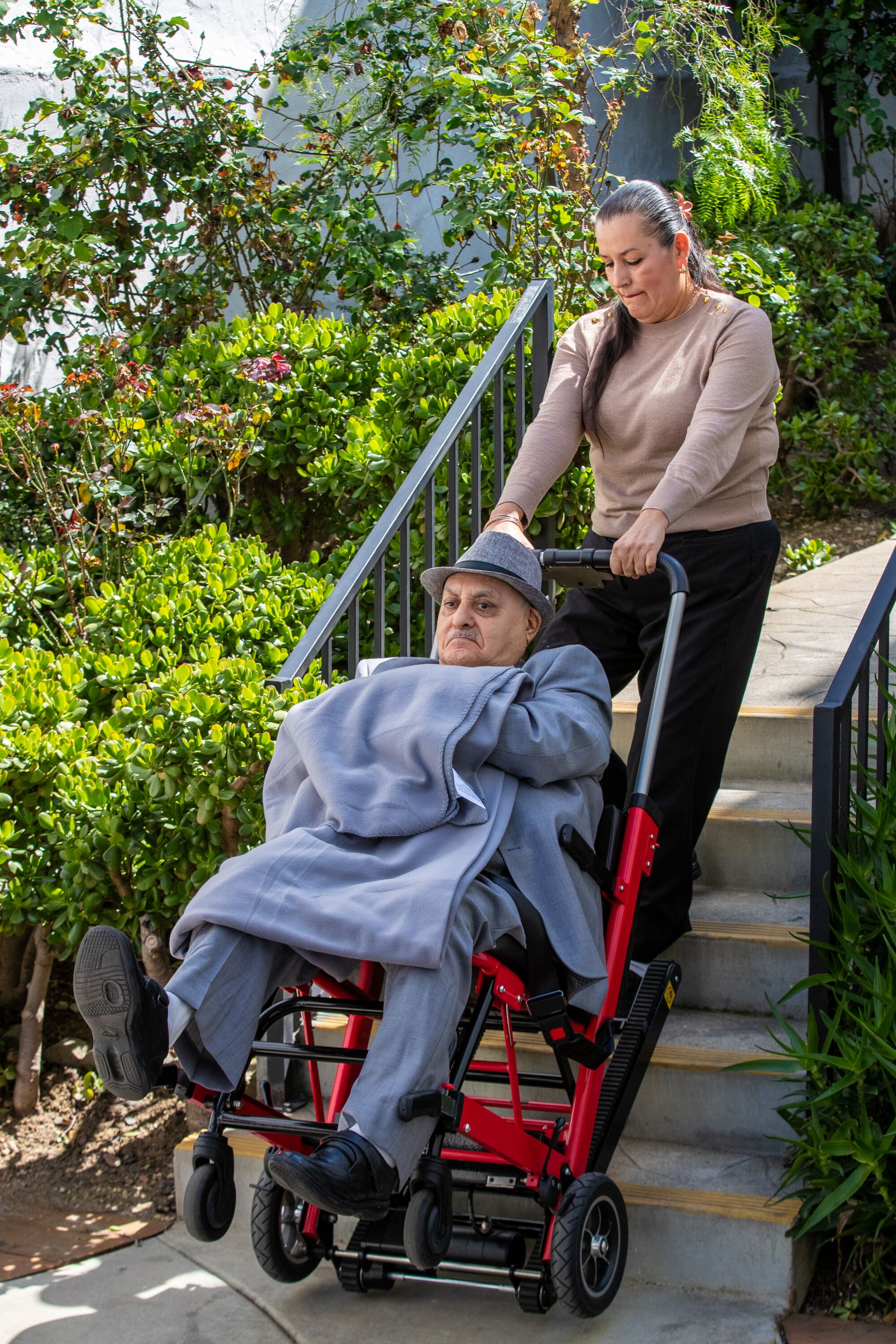  Patricia Santana pulls Ismael Anguiano, seated on a wheel-chair dolly, up a set of stairs.