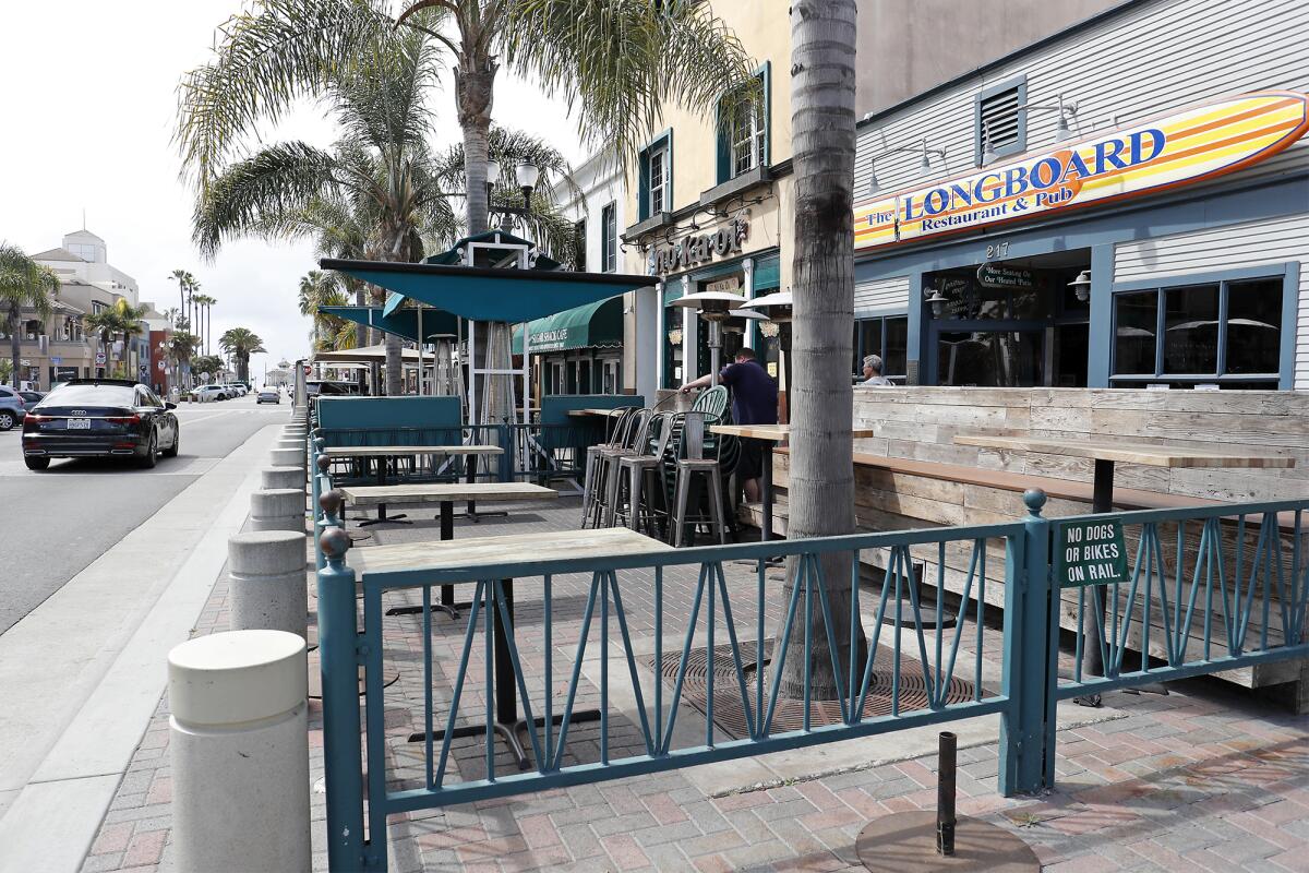An employee locks up chairs in the outdoor patio seating area at Longboard Restaurant and Pub in a quiet downtown Huntington Beach on Thursday. Onsite dining has been curtailed throughout Orange County as a protective measure against the spread of the coronavirus.