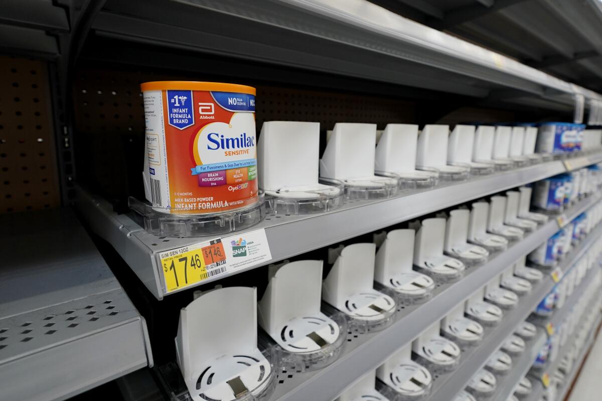 A few cannisters of baby formula sit on mostly empty grocery store shelves