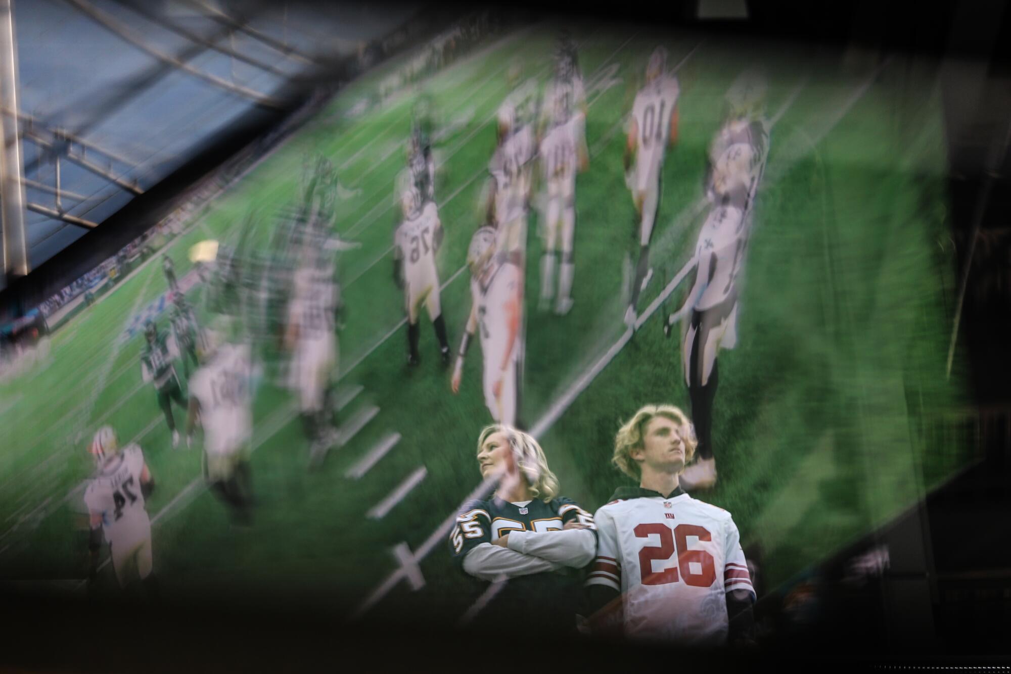 Reflection of a game between the Saints and the Jets is reflected on a plexiglass barrier, as fans arrive to the field.