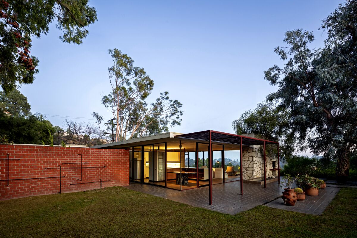 To the rear, a steel pergola, painted burgundy (a color used throughout), extends from the home’s fascia; a squat brick wall is fitted with climbing bars.