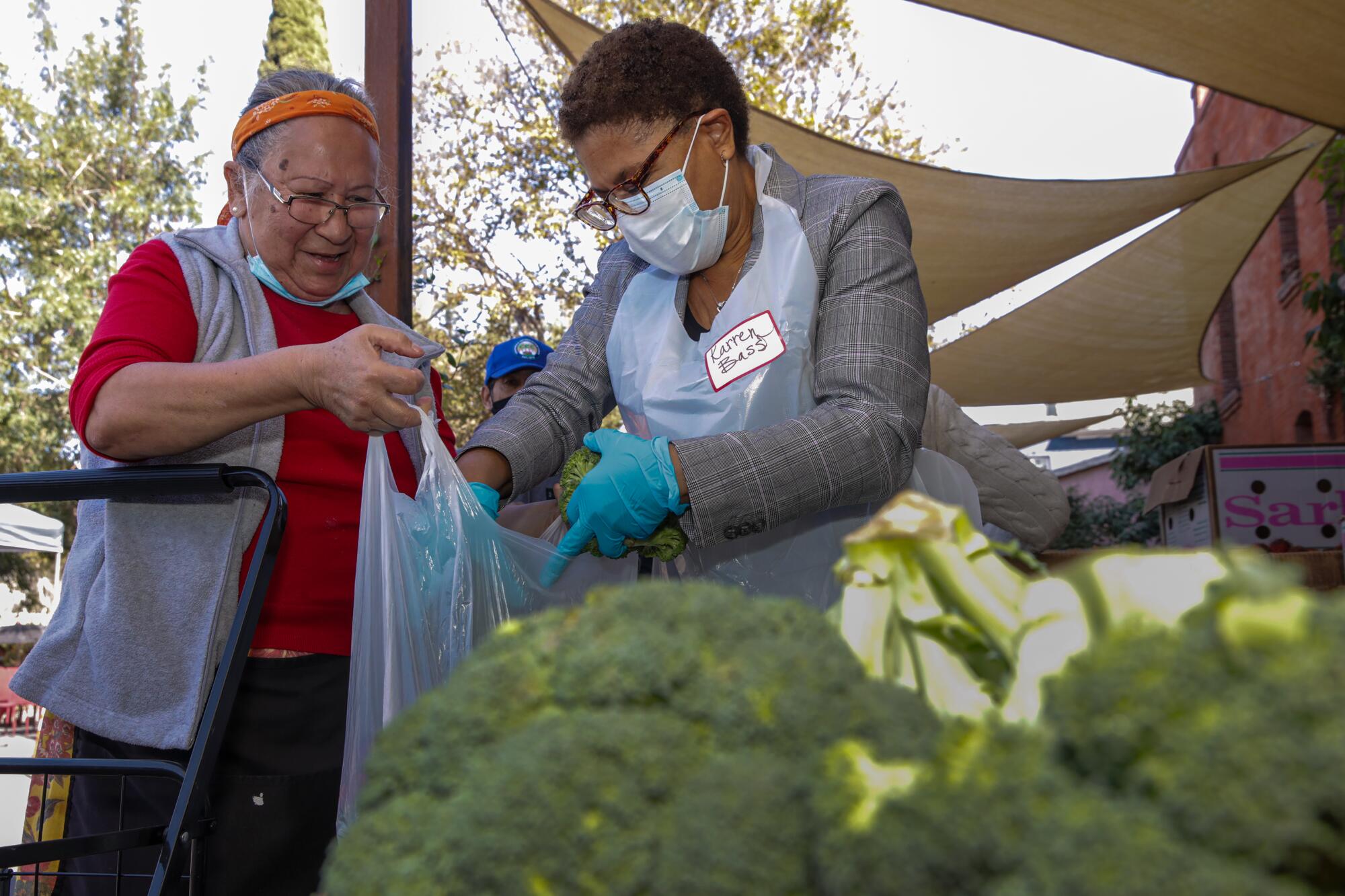 Karen Bass, right, distributes produce to a woman at a farmers market.