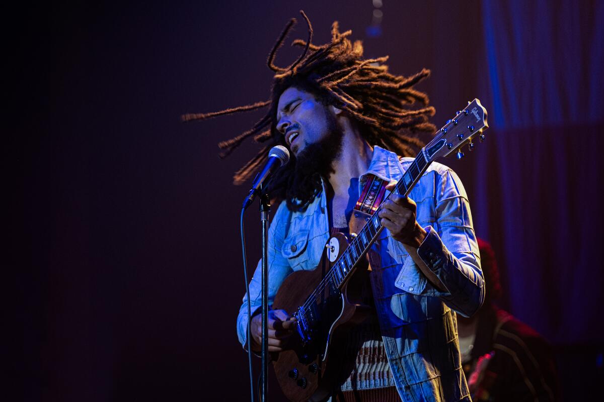 A performer with dreadlocks plays guitar and sings into a microphone.