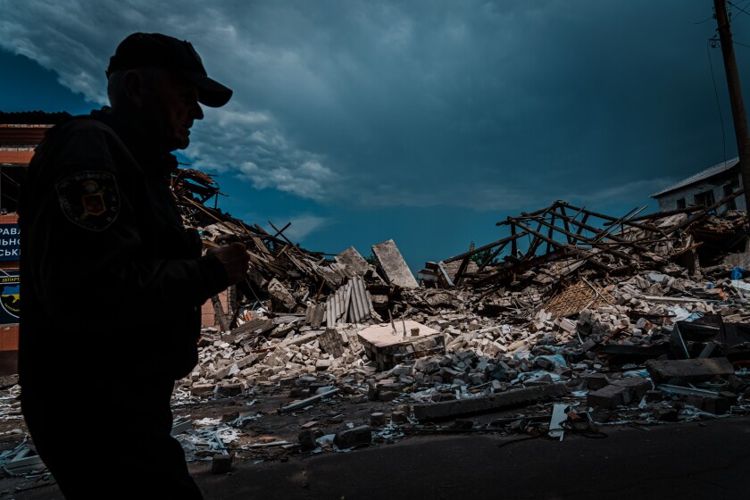 A man in profile walks by rubble