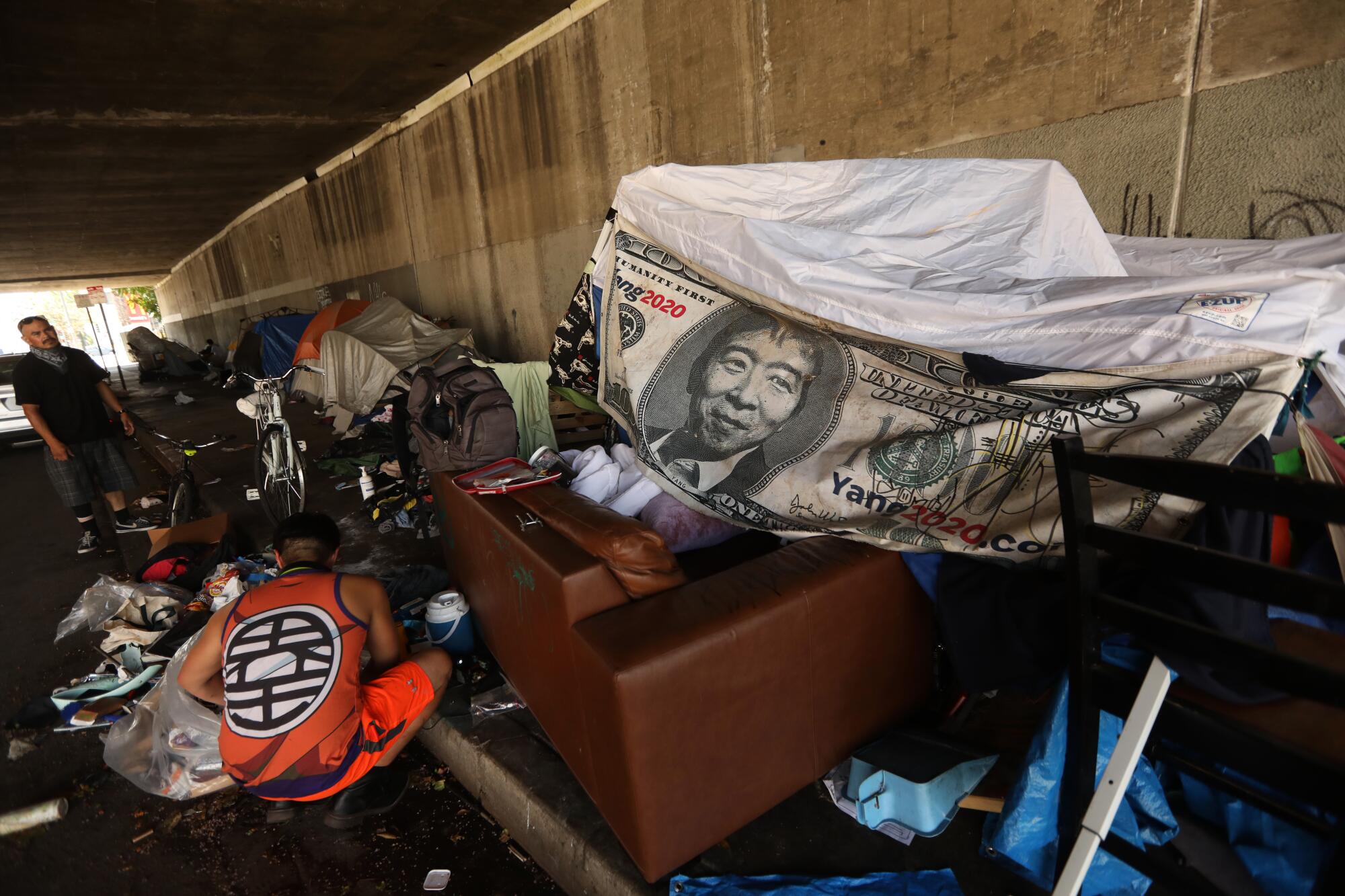 A banner depicting Andrew Yang on a $1,000 bill helps provide shelter in an encampment under the 134 Freeway.