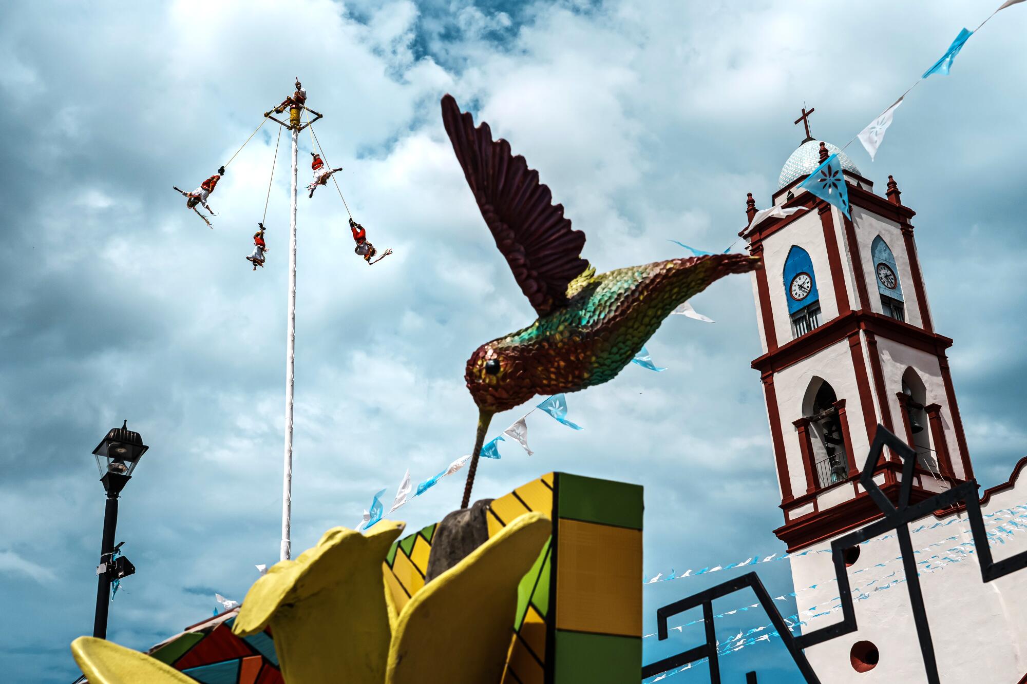 Voladores fly off a metal pole as they perform to a tourist crowd lingering outside the church in Papantla, Mexico