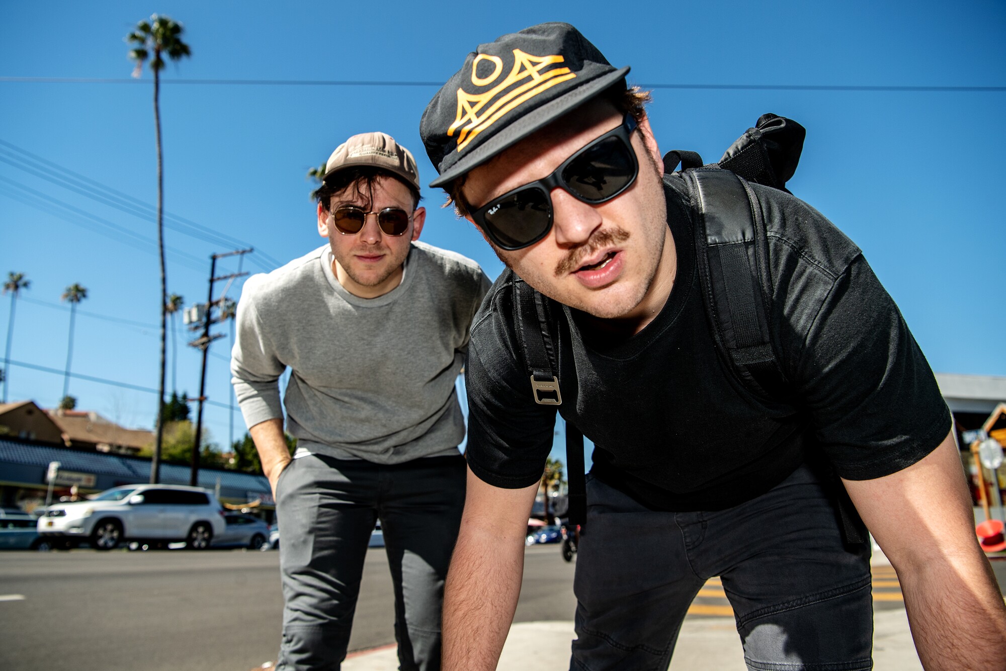 Brooke Palmieri and Zachary Weathers wear sunglasses and crouch down on Sunset Boulevard.